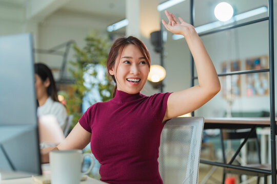 freshness business office woman staff hand gesture wave say hi to her colleague while sit work at desk smiling happiness female woman working in modern interior office space hand greeting casual girl