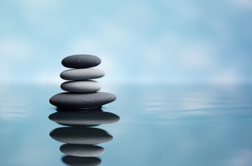  Balanced stack of black pebbles creating the illusion of circles in calm water, set against a light blue and white background with ripples.