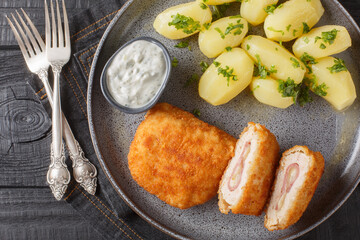 French Schnitzel Cordon bleu, filled with ham and cheese with new potatoes and cream sauce closeup on the plate on the table. Horizontal top view from above