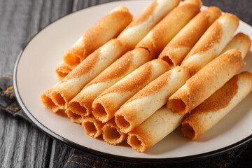 Thin wafer tubes baked to a crispy golden crust are called Russian cigarettes close-up in a plate on the table. Horizontal