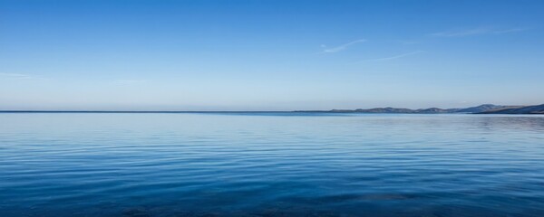 A serene calm body of water reflecting the clear blue sky, with distant mountains visible on the horizon