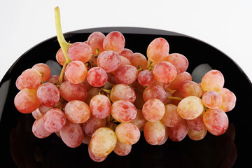 A juicy beautiful bunch of grapes lies in a black plate.