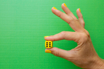 Woman's hand holding a yellow die with the number six on it