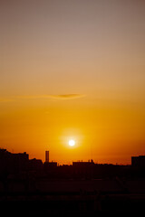 The bright, warm yellow sun hangs over the city's dark silhouette during sunset, creating a beautiful landscape in the evenings.