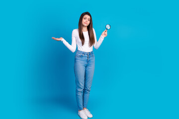 Full size photo of pretty teen girl magnifier loupe shrug shoulders wear trendy white outfit isolated on blue color background