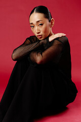 Asian woman in black top and pants sitting on red background with hands on knees