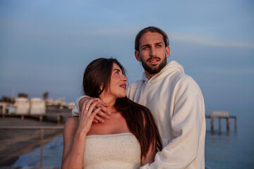 Beautiful young couple of fiancés hugging and exchanging gestures of love during a solitary outing to the sea at sunset