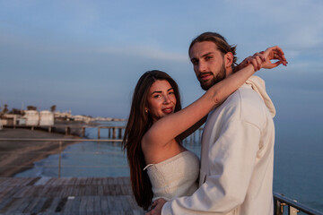 portrait of a young charming and sensual couple of engaged lovers while they embrace each other with love and passion while they are at the seaside during the sunset