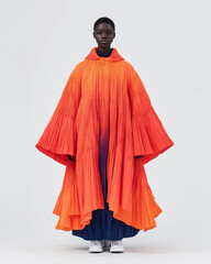 Full-body shot of an African model wearing a blue-to-orange ombre oversized cape dress with pleats, in a high-fashion streetwear style , minimalistic, hyper-realistic photography