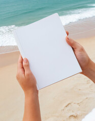 People hands holding a white book mock-up with copy space in front of a beautiful beach , woman read a book on the beach in summer concept image
