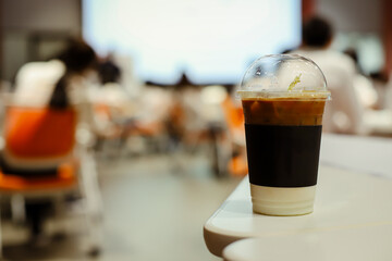 Close up glass of ice latte with blurred people in business workshop and presentation.Beverage at the conference room.