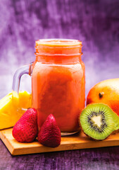 Tropical Fruit Smoothie with Mango, Strawberry, Kiwi and pineapple served in mug isolated on wooden board closeup side view of antioxidant juice