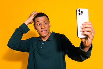 Photo portrait of nice young male hold device confused wear trendy green outfit isolated on yellow color background