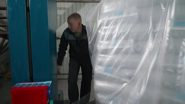 Worker checking on the product batch wrapping process at the facility. Wrapping the product batch with plastic material. Wrapping product batch manufactured at the industrial plant.