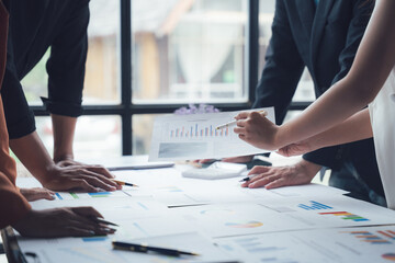 Strategic Collaboration: A diverse team of business professionals collaborates around a table, analyzing charts and graphs in a modern office setting. This image embodies teamwork, data analysis.