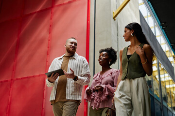 Low angle shot of diverse team of three smiling coworkers discussing business matters while walking...