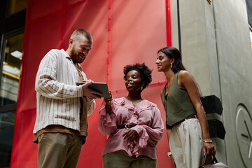 Medium shot of diverse group of three workers discussing business matters while looking at digital tablet screen during meeting in hallway of modern office center, copy space