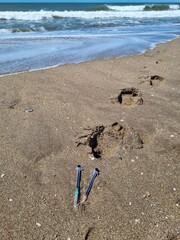 Syringes in the sand with waves in the background