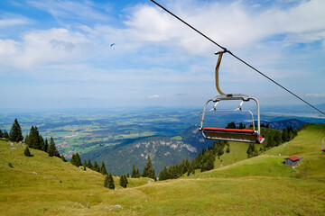 scenic alpine view with a cableway with red chairlift over the Bavarian Alps and lake Forggensee and a paraglider in the background, seen from Breitenberg mountain (Pfronten, Bavaria, Germany)	