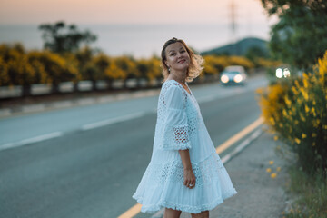 A woman in a white dress is standing on the side of a road