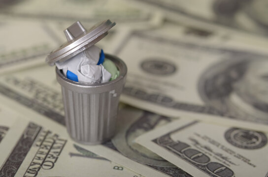 The image depicts a miniature trash can filled with crumpled paper money, symbolizing the concept of wasted money or financial loss.