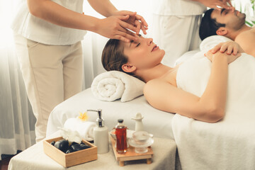 Caucasian couple enjoying relaxing anti-stress head massage and pampering facial beauty skin recreation leisure in dayspa modern light ambient at luxury resort or hotel spa salon. Quiescent