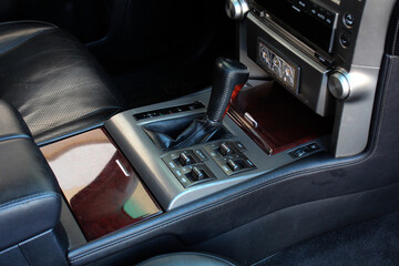 Automatic transmission gear shift knob. Black leather interior of luxury SUV. Wood trim in the...