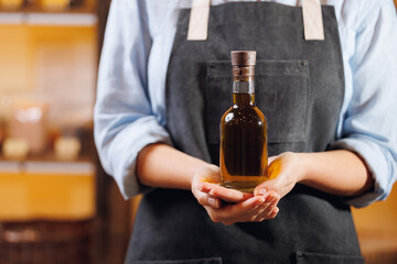 Craft master in apron holds bottle with fresh oil from hemp cannabis seeds