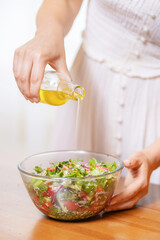 Closeup of young woman hands pouring craft extra virgin oil sunflower into fresh salad. Concept eco nature and wholesome food vegetarian