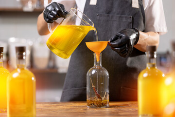 Master in apron bottling craft sunflower oil with red pepper spices in glasses bottle on workplace...