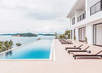 Fototapeta premium Luxurious villa with an infinity pool overlooking serene waters and lush islands on a cloudy day