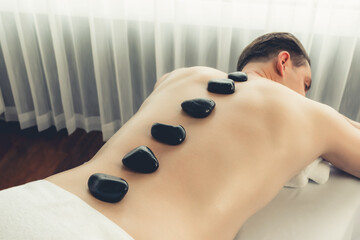 Hot stone massage at spa salon in luxury resort with day light serenity ambient, blissful man...