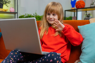 Preteen child girl looking at laptop camera, making video webcam conference call with friends or family enjoying pleasant conversation. Teenager little female kid at home living room apartment on sofa