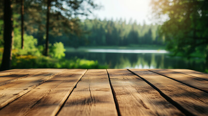 Pusty drewniany stół z lekkimi rysami i ciepłym odcieniem znajduje się na pierwszym planie, a w tle majestatycznie rozciąga się letnie jezioro otoczone gęstym, zielonym lasem. 
