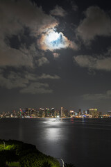 Fototapeta premium Moonlight reflecting on San Diego bay with city skyline in background. Vertical view.
