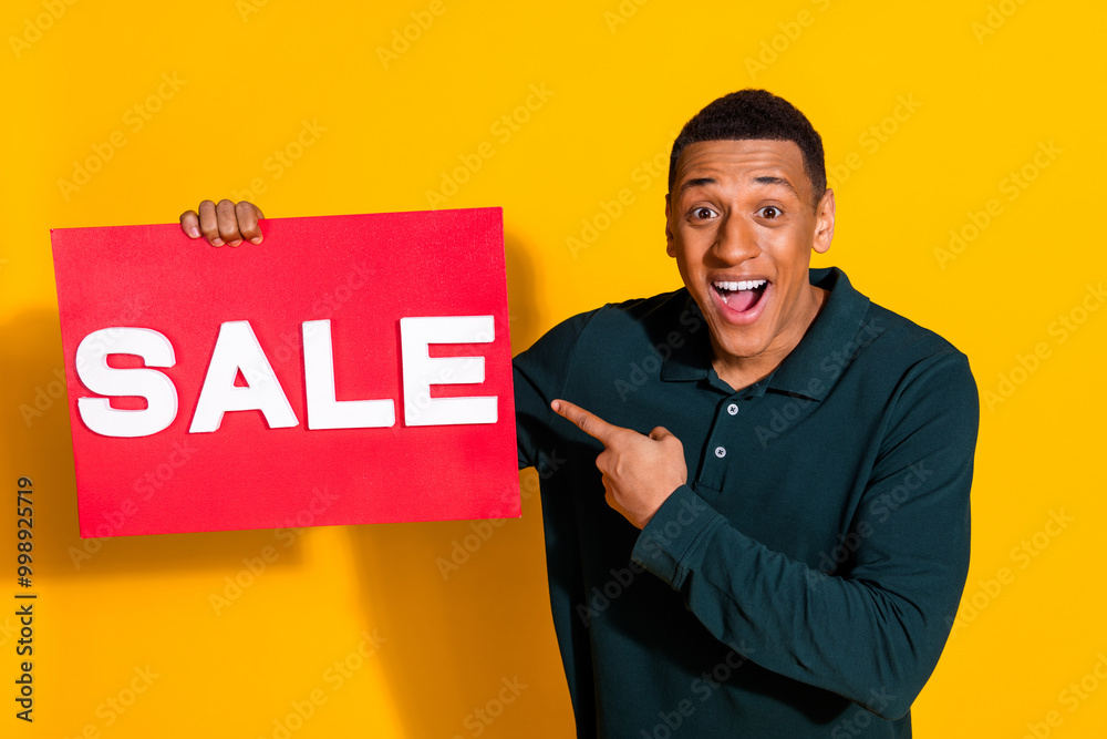 Poster Photo portrait of attractive young man hold sale point plate excited dressed stylish green clothes isolated on yellow color background