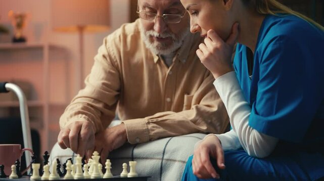 Elderly man teaching his young caregiver how to play chess game, assisted living