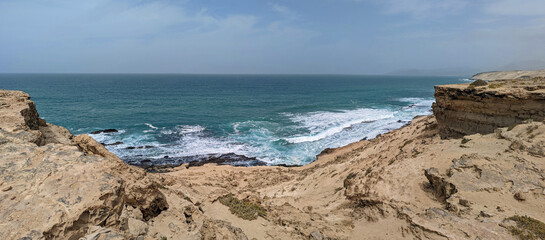 Panoramic view of the sandy slopes and cliffs of the rocky west coast of the island of Furteventura in the Canary Islands under a blue cloudy sky
