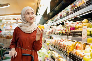 Young muslim woman enjoying her time shopping at the grocery while holding orange fruit