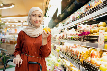 Young muslim woman enjoying her time shopping at the grocery while holding orange fruit
