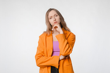 thoughtful and concerned young woman with a serious expression looking at the camera. Concept of introspection and concern. Female posing on a white studio background, wearing an orange blazer