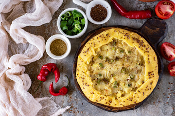 An open pie with potatoes and green onions on a gray background. Vegetarian pie. View from above. Close-up.