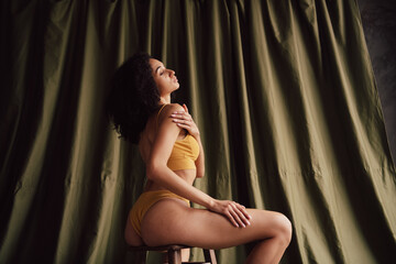 Obraz premium Unretouched portrait of gorgeous model girl sit chair touch shoulder khaki curtain background