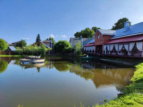 Gorodets, Russia - July 02, 2023: A serene setting in Gorodets, Russia, featuring a calm pond surrounded by charming cabins under a bright blue sky