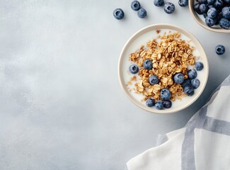 granola with blueberries and milk in a bowl on a light grey background, top view. healthy breakfast with a bowl of milk and wheat grass cereal with fresh fruits for a balanced meal concept.