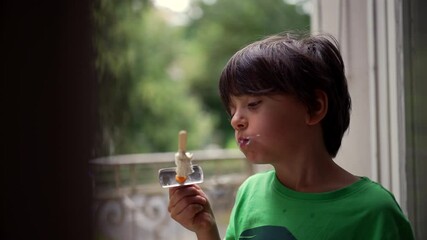 Young boy eating ice cream outdoors, biting into a popsicle while enjoying a sweet treat. Joyful expression as the child savors the dessert on a warm day