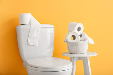 Ceramic toilet bowl and rolls of paper near color wall
