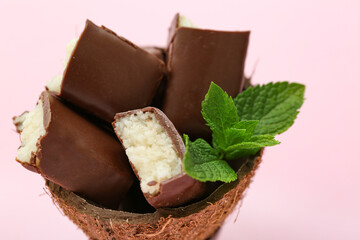 Coconut shell with tasty chocolate covered candies on pink background