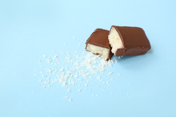 Halves of tasty chocolate covered coconut candy on blue background