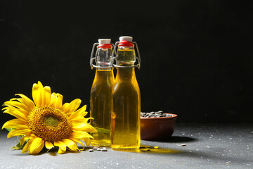 Bottles of sunflower oil and bowl with seeds on black background